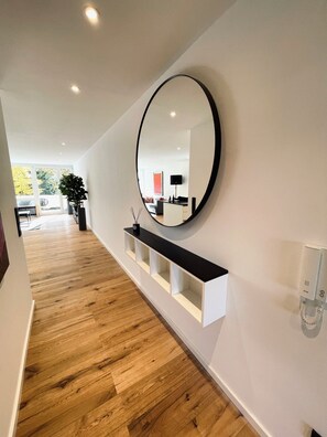 A hallway with a wooden floor, a black-framed mirror, and a white console table. - MY STAY - Relaxation by the Lake with a Sauna & Swimming Pool (Prien am Chiemsee)