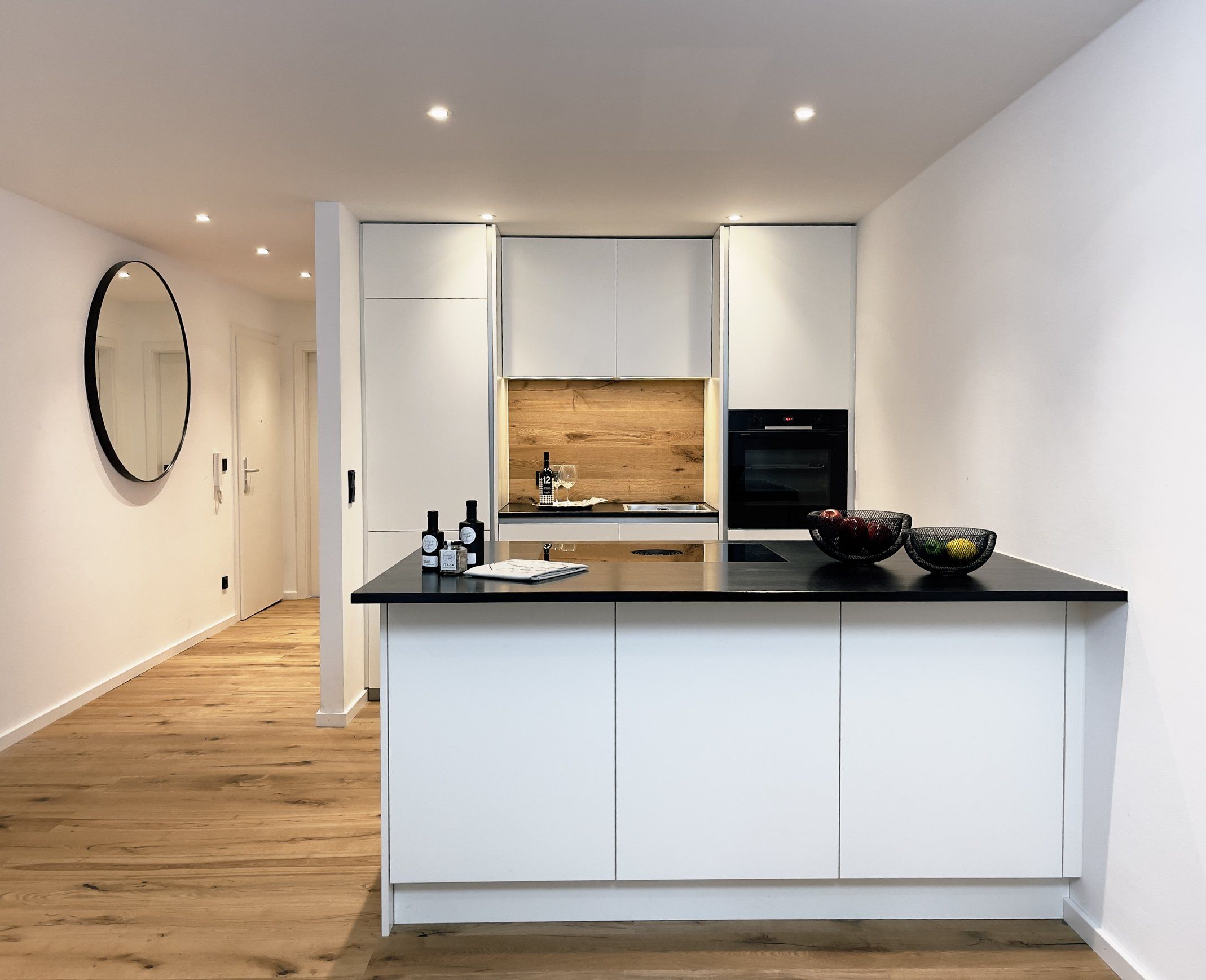 Une cuisine moderne avec des meubles blancs, un plan de travail noir et un pare-feu en bois.