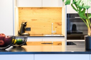 A kitchen with a wooden backsplash, a coffee maker, and a bowl of fruit on the counter. - MY STAY - Relaxation by the Lake with a Sauna & Swimming Pool (Prien am Chiemsee)