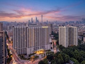 Un edificio de gran altura con varios pisos, rodeado de otros edificios altos, y un cielo despejado con un atardecer.