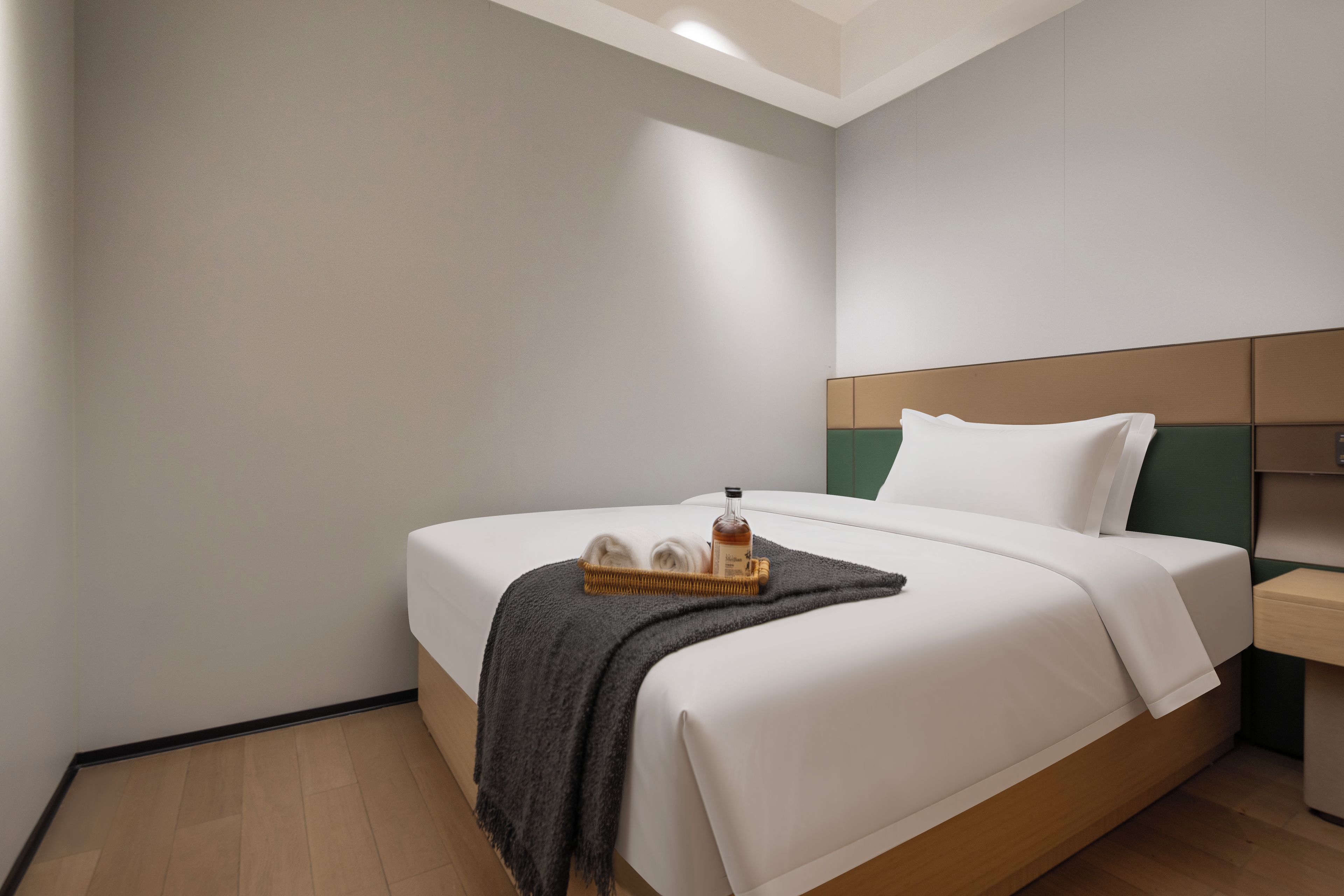 Habitación de hotel con una cama individual, una mesita de noche, una botella de licor y una bandeja con pantuflas.