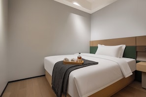 Habitació d'hotel amb un llit ben fet, una taula de nit amb una ampolla i un safata amb xapes.