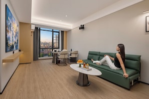 Un saló modern amb un sofà verd, una taula de centre i vista a la ciutat a través de grans finestres.