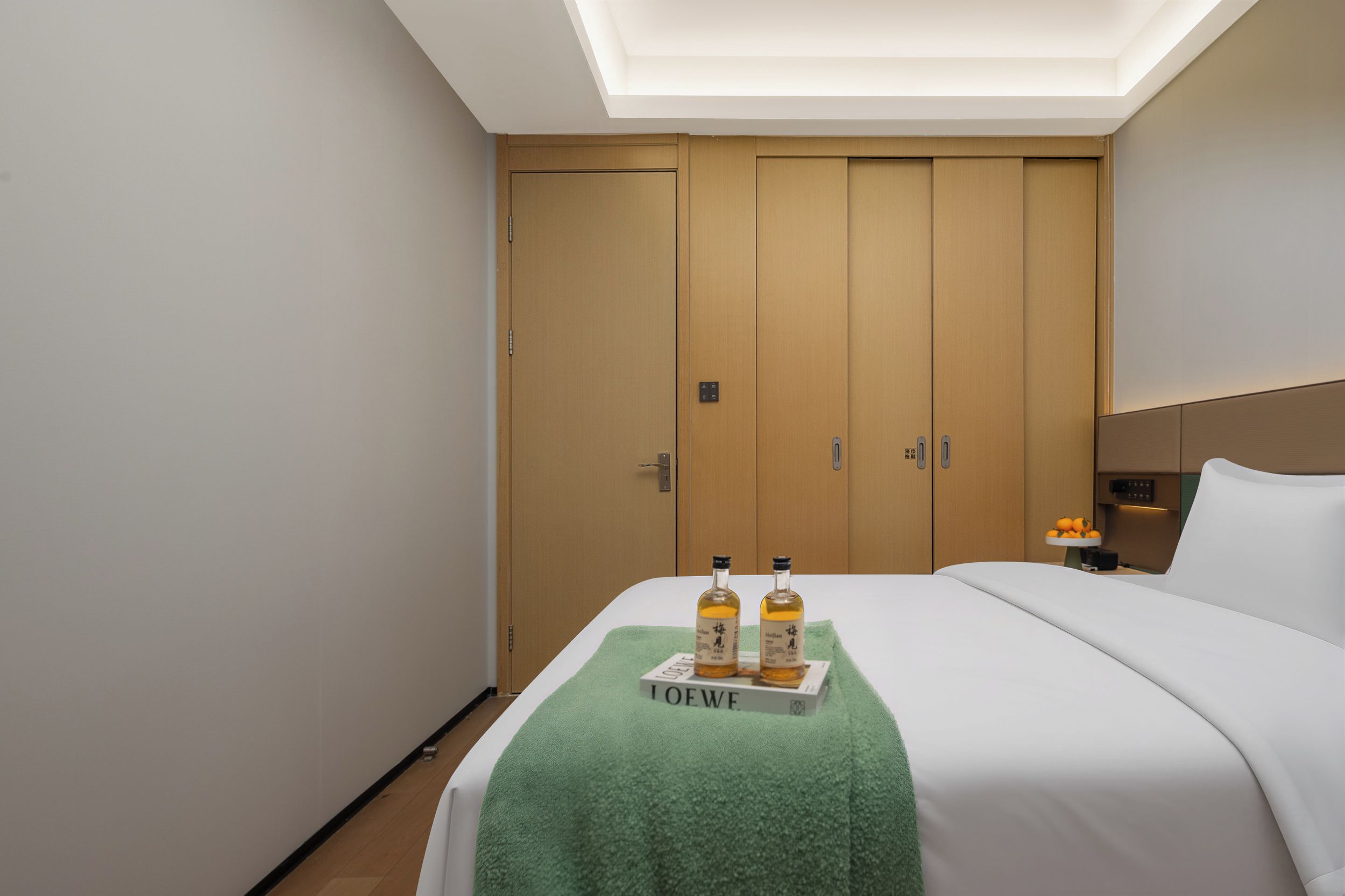 Ein Hotelzimmer mit einem Bett, einem Nachttisch, einem grünen Handtuch und zwei Flaschen auf einem Tablett.