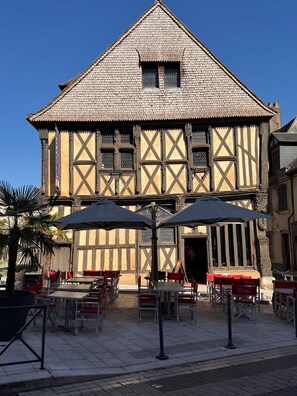 A traditional half-timbered building with a gabled roof and a small window. In front, there are outdoor tables and chairs under umbrellas, suggesting a café or restaurant setting. - Charming House in Berry · Near Sancerre · Eco-Friendly. Take a breath. (Sury-ès-Bois)