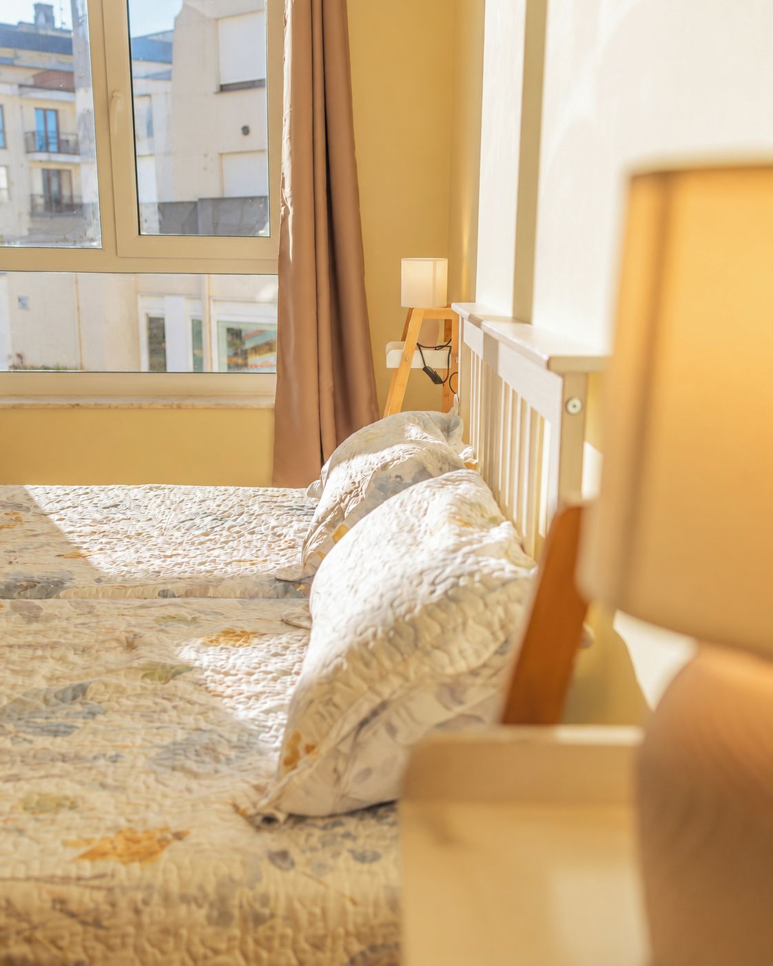 Un dormitorio con una cama, una mesita de noche, una lámpara y una ventana con cortinas.