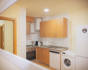 A compact kitchen with wooden cabinets, a built-in washing machine, and a dishwasher.