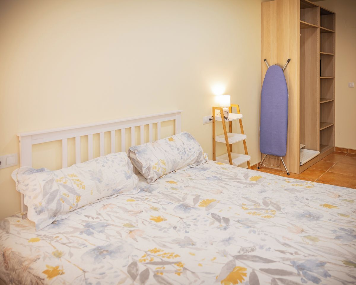 Un dormitorio con cama, mesita de noche, lámpara y armario de madera.