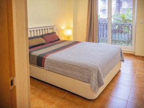 A bedroom with a bed, a nightstand, a lamp, and a view of the outside.
