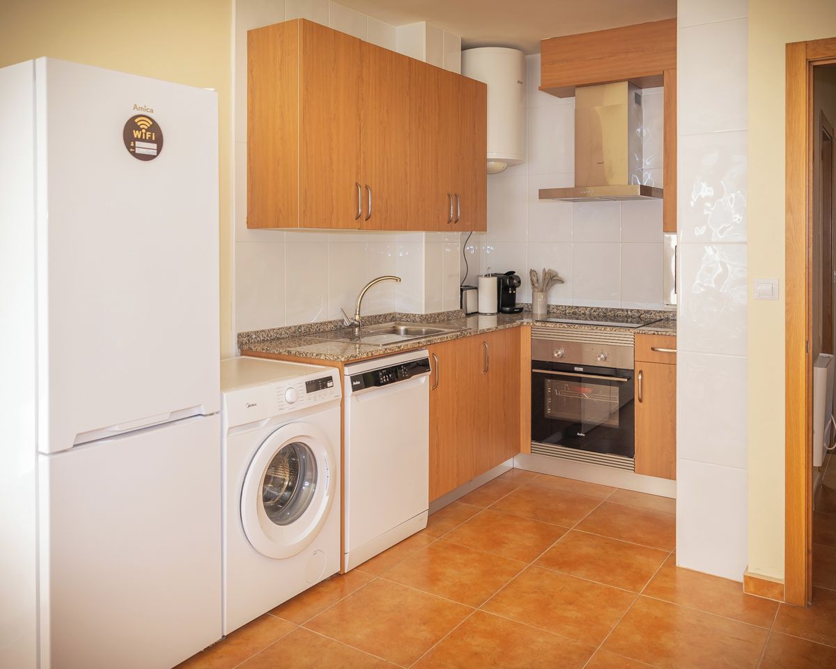 Een compacte keuken met een wasmachine, vaatwasser, oven en een inbouwmagnetron.
