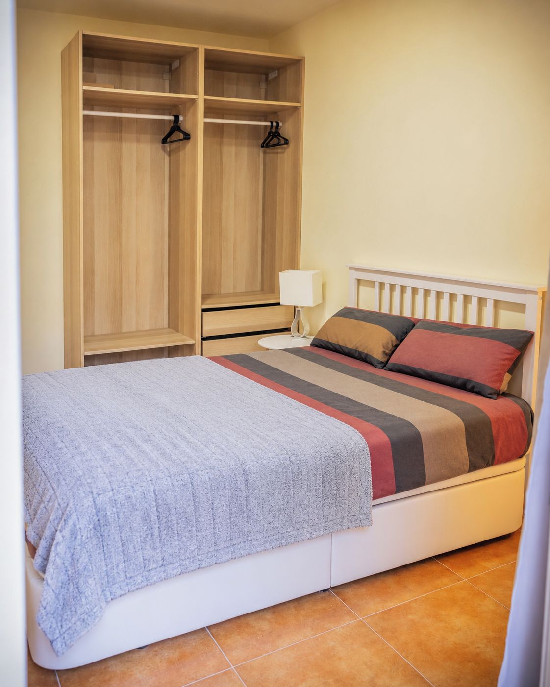 Quarto com cama, mesa de cabeceira, luminária e guarda-roupa de madeira.
