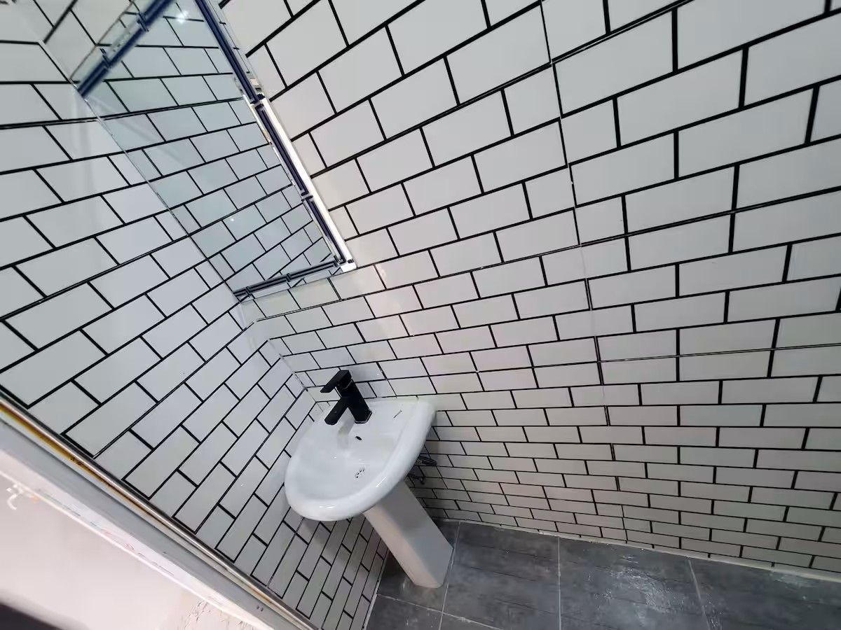 Casa de banho com paredes em azulejo branco e lavatório pedestal branco.