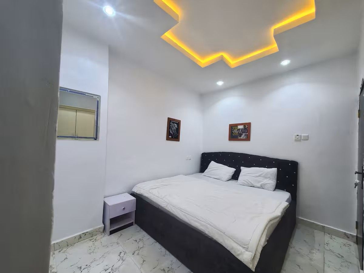 Quarto com cama, mesa de cabeceira e luminária no teto.