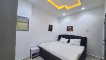 Quarto com cama, mesa de cabeceira e luminária no teto.