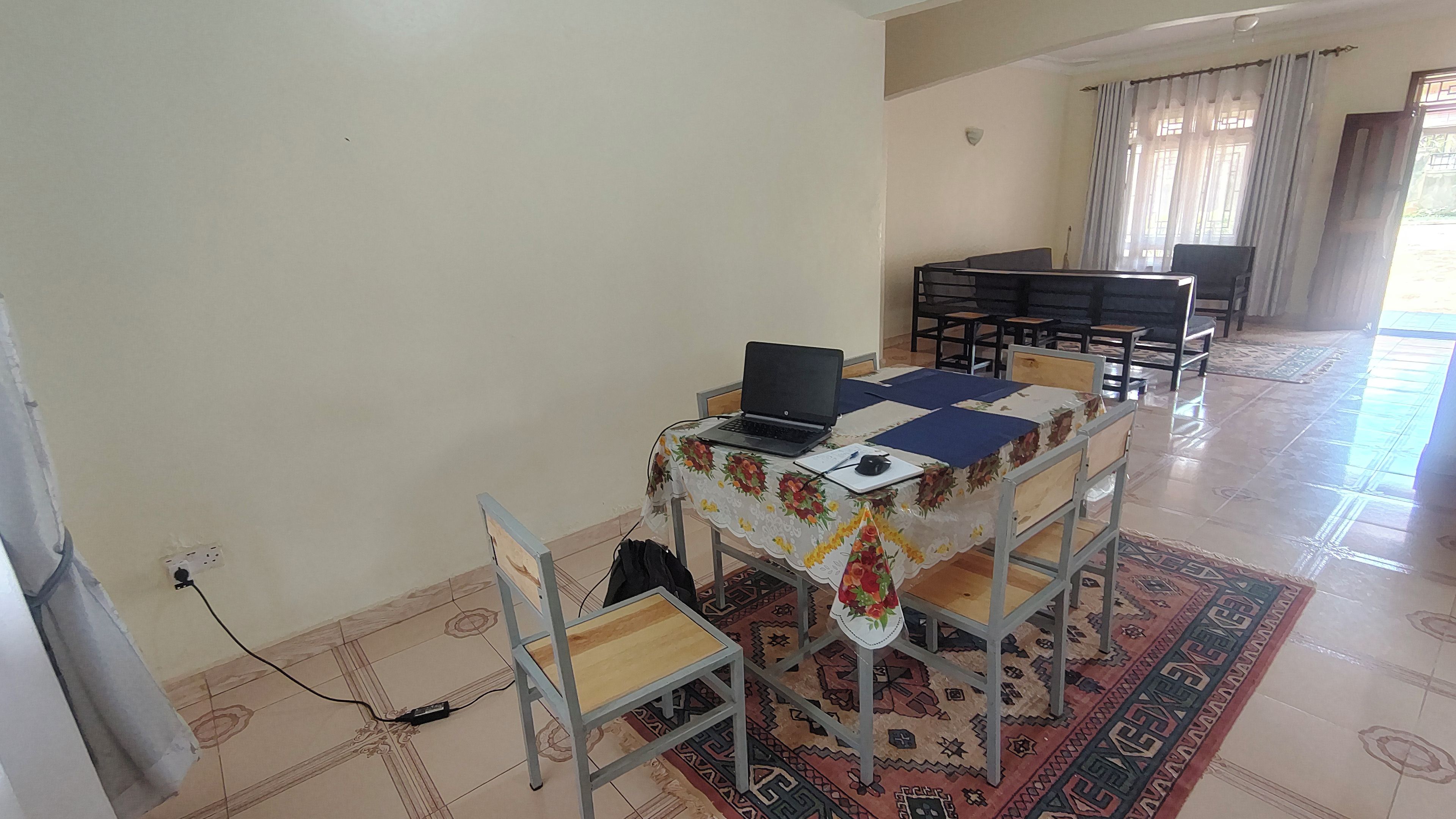 Un comedor con una mesa preparada para dos personas, una computadora portátil sobre la mesa y un tapete estampado en el suelo.