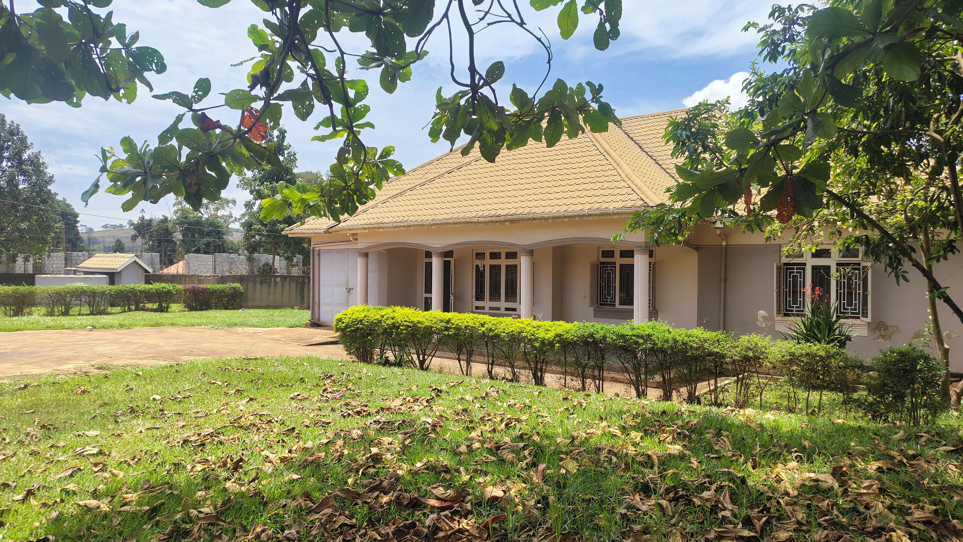 A single-story house with a tiled roof, a covered porch, and a well-maintained lawn with a hedge in the foreground.