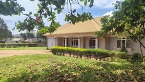 A single-story house with a tiled roof, a covered porch, and a well-maintained lawn with a hedge in the foreground.