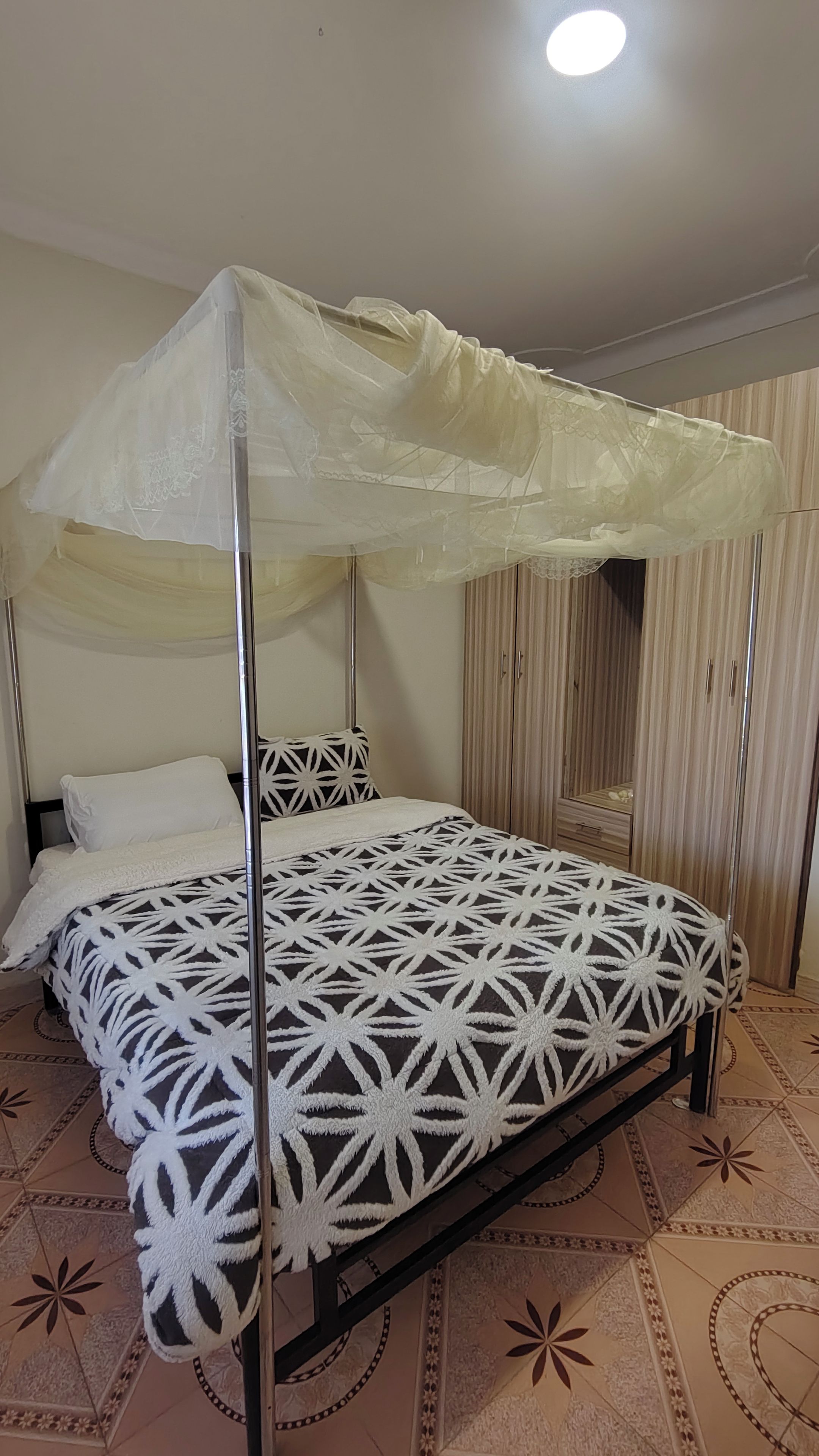 Ein Himmelsbett mit einem geometrisch gemusterten Bettbezug, ein Nachttisch und ein Kleiderschrank mit vertikalen Streifen.