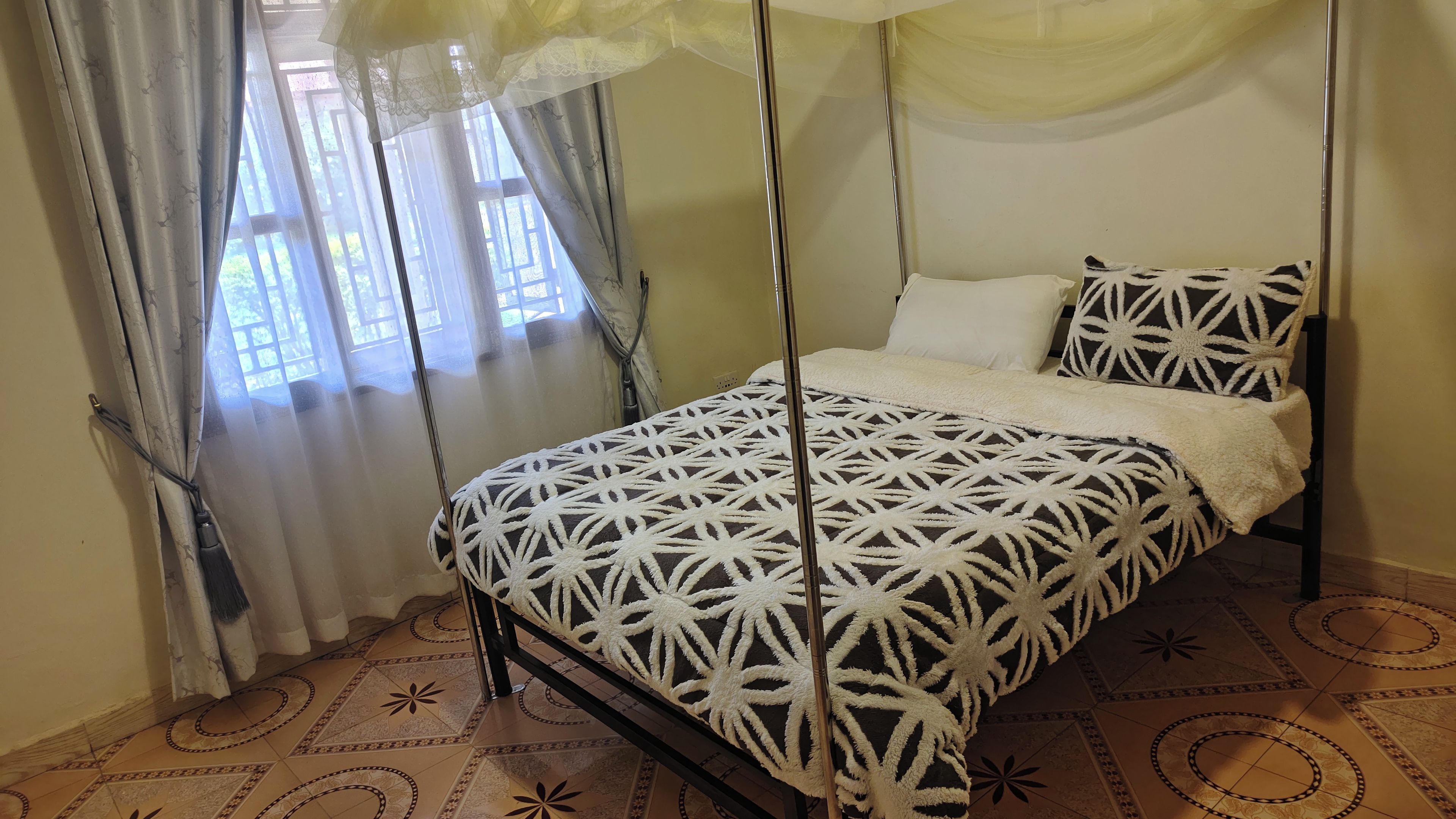 A bed with a geometric patterned bedspread, a canopy, and a window with curtains.
