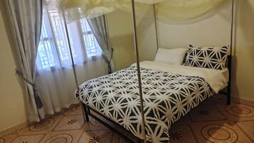 A bed with a geometric patterned bedspread, a canopy, and a window with curtains.