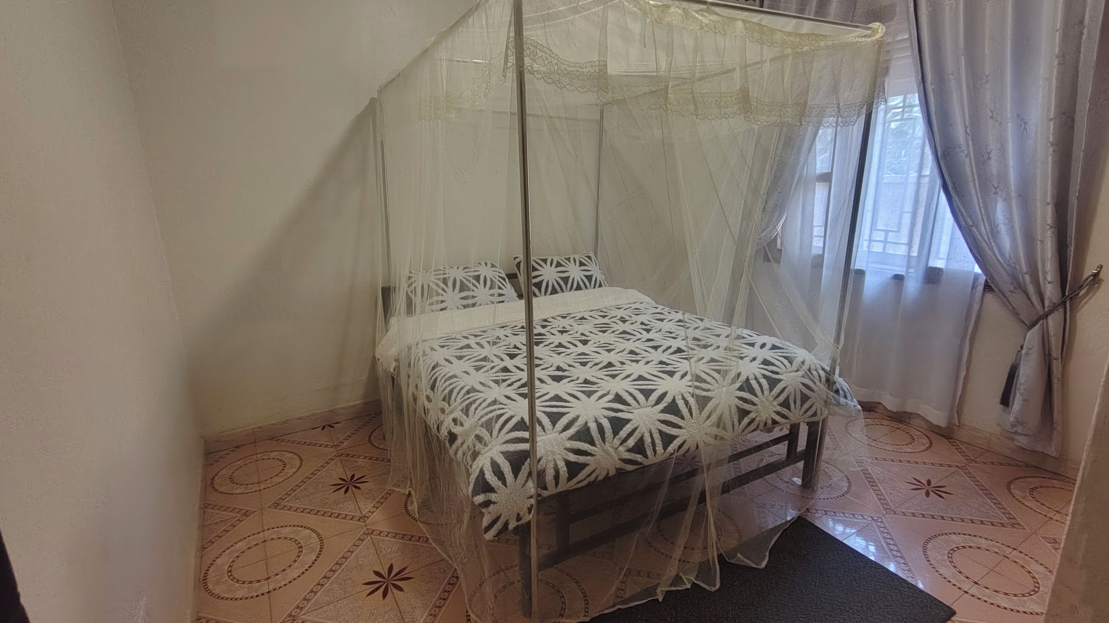 A room with a bed under a canopy, a patterned floor, and a window with curtains.