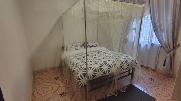 A room with a bed under a canopy, a patterned floor, and a window with curtains.