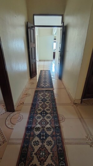 A hallway with a patterned carpet, wooden doors, and tiled flooring.