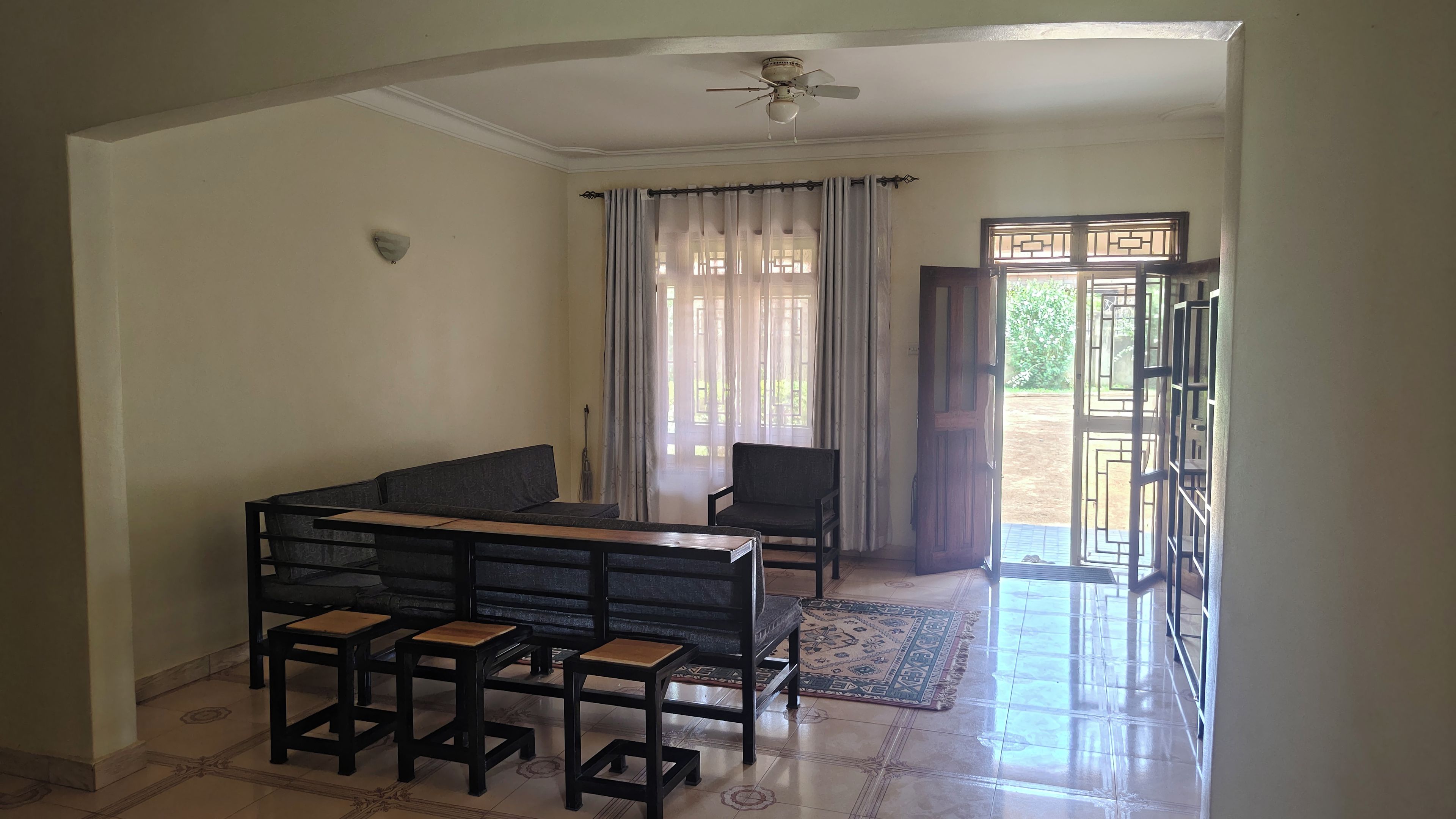 A room with a dining table, chairs, a sofa, a ceiling fan, and a view through a door to an outdoor area.