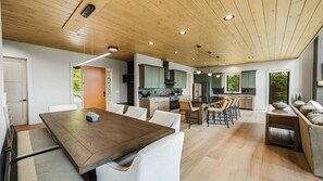 Eine moderne Küche mit einer Kochinsel, einem Essbereich mit Holztisch und -stühlen sowie einer gemütlichen Sitzecke mit Sofa und Beistelltisch.