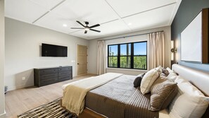 Quarto com cama, cômoda, ventilador de teto, televisão e janela com vista.