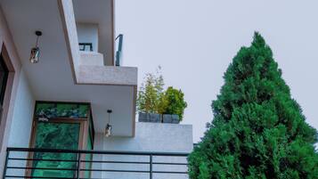 A modern building with a balcony, a large window, and a green tree in front.
