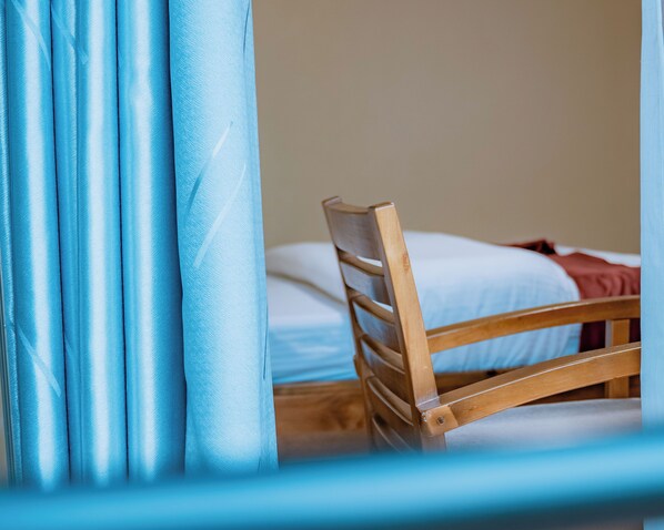A wooden chair with a slatted backrest positioned next to a bed with white bedding.