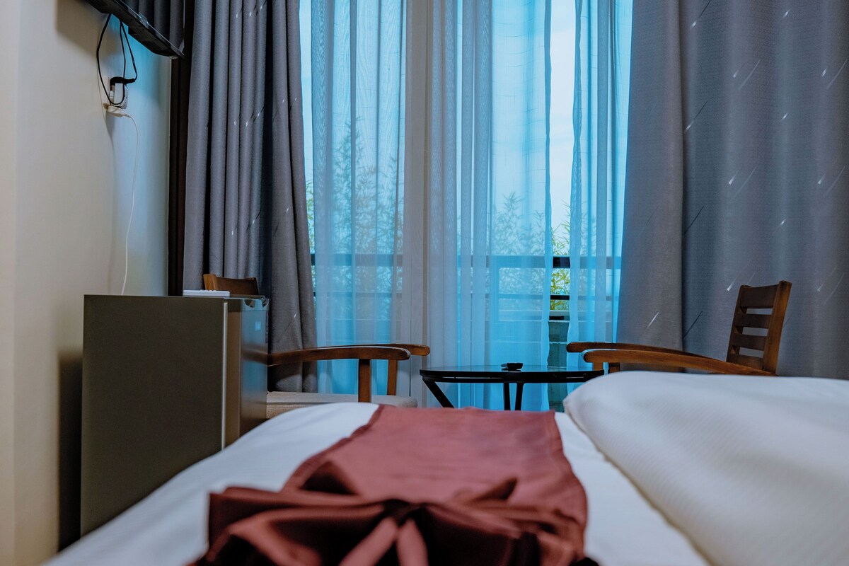 Une chambre d’hôtel avec un lit, un bureau, une chaise et une fenêtre avec des rideaux.
