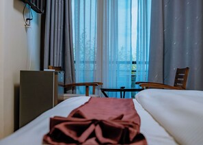 A hotel room with a bed, a desk, a chair, and a window with curtains. - VELVET SUITES - KIMIRONKO (Kigali)