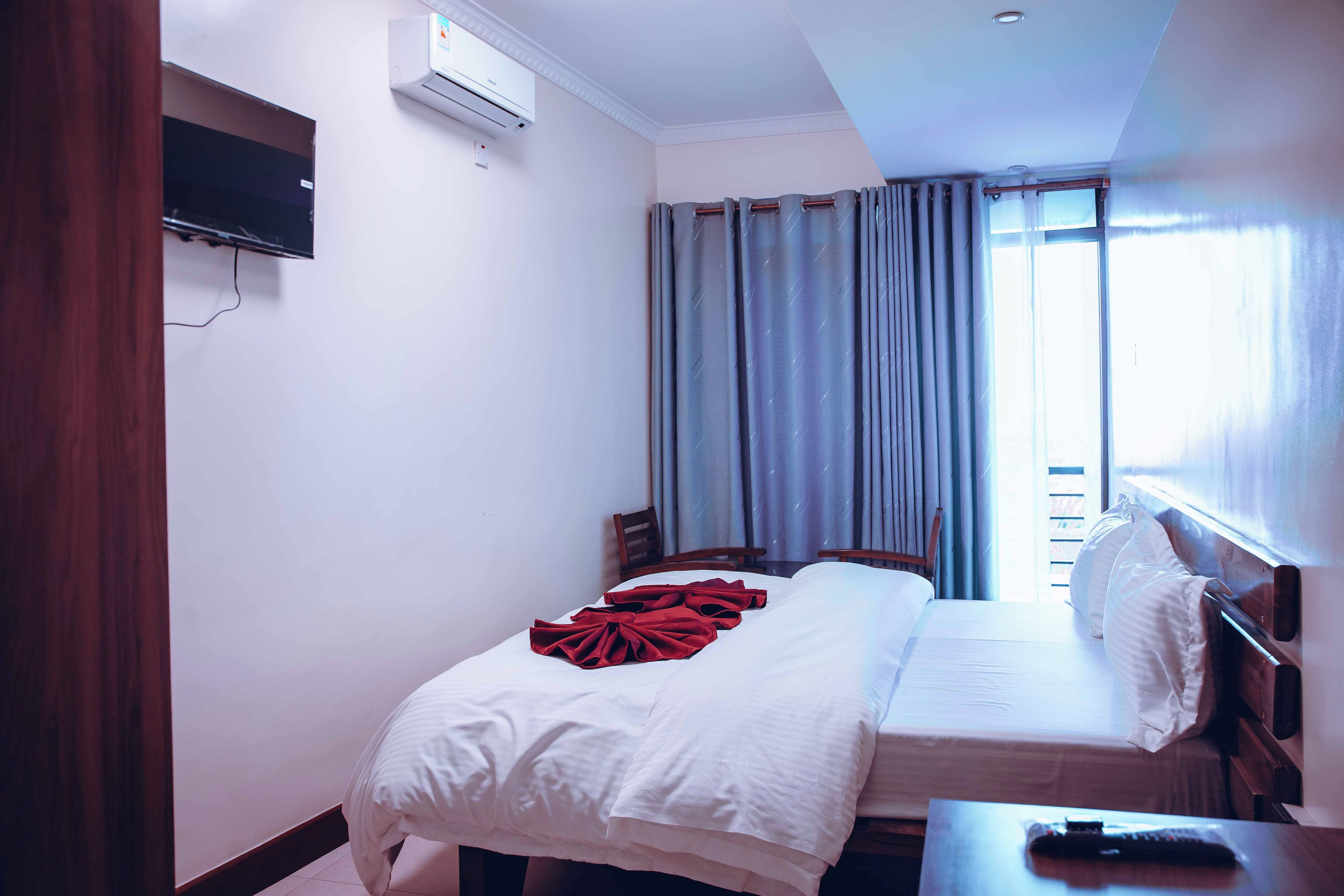 A hotel room with a bed, a TV mounted on the wall, and a window with curtains.