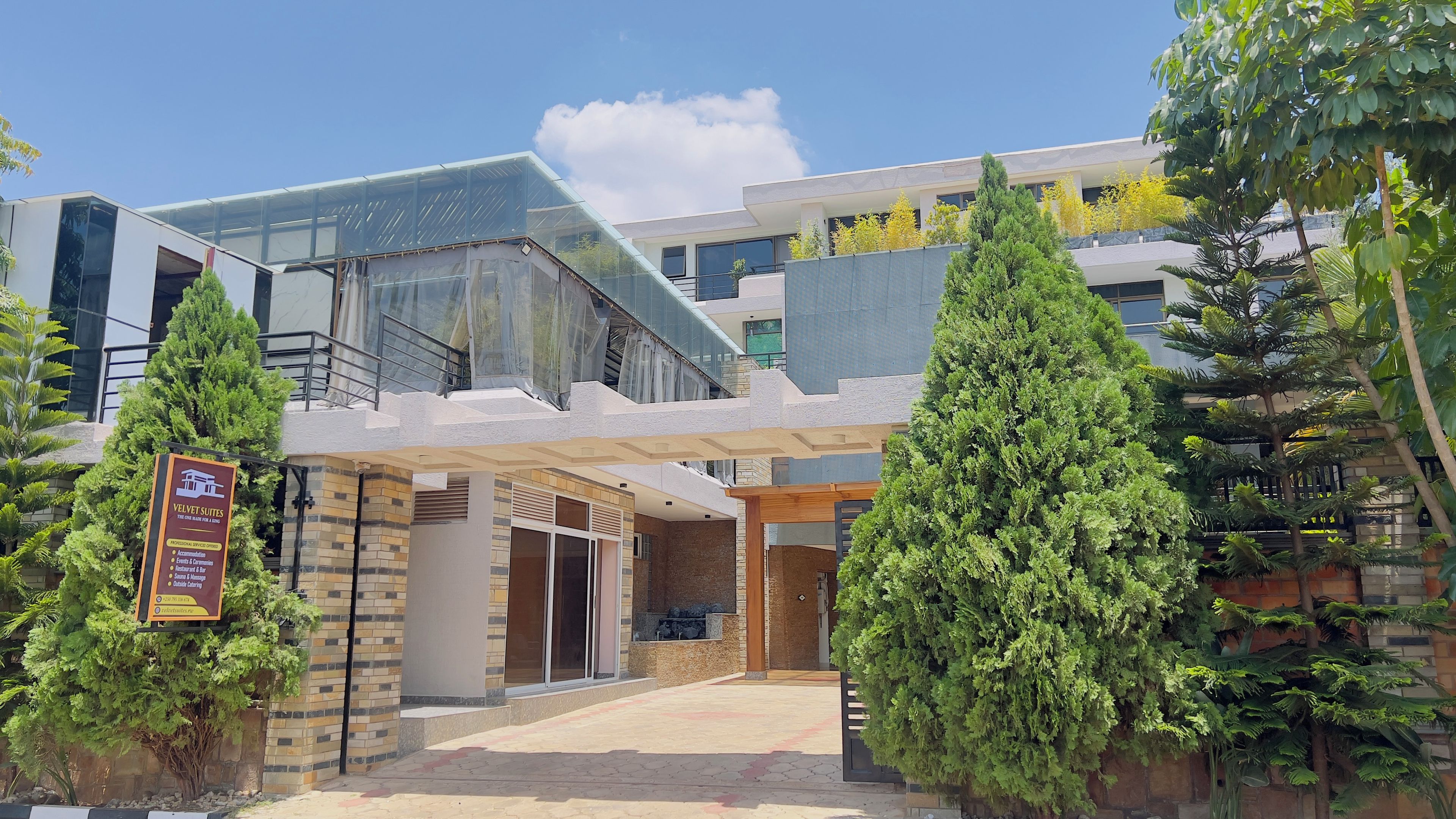 A modern hotel entrance with a glass facade, a brick exterior, and a signboard advertising services.
