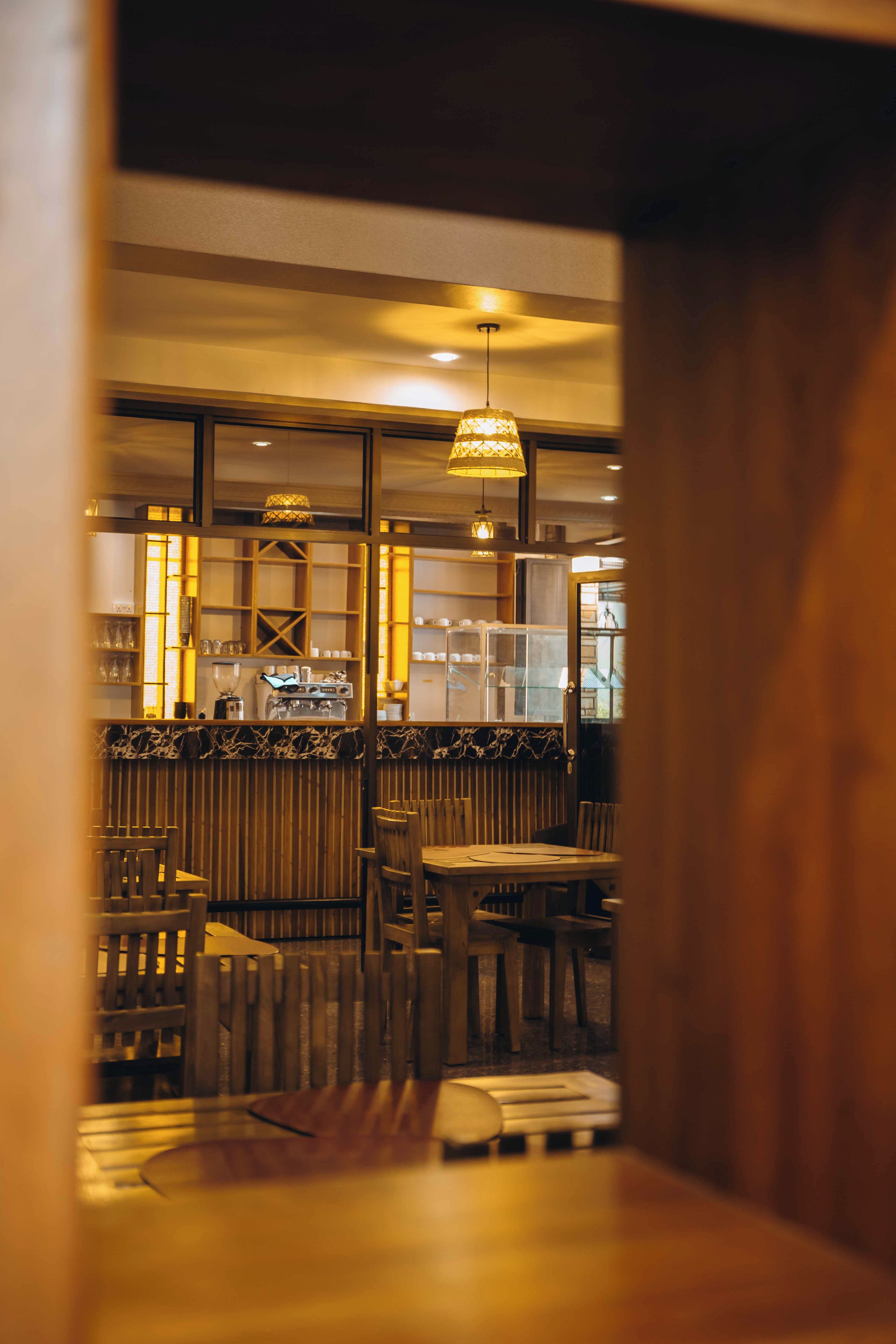 An interior view of a restaurant with wooden furniture, a bar area, and hanging pendant lights.