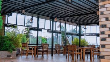 Un comedor interior con mesas y sillas de madera, ventanas amplias y faroles colgantes.