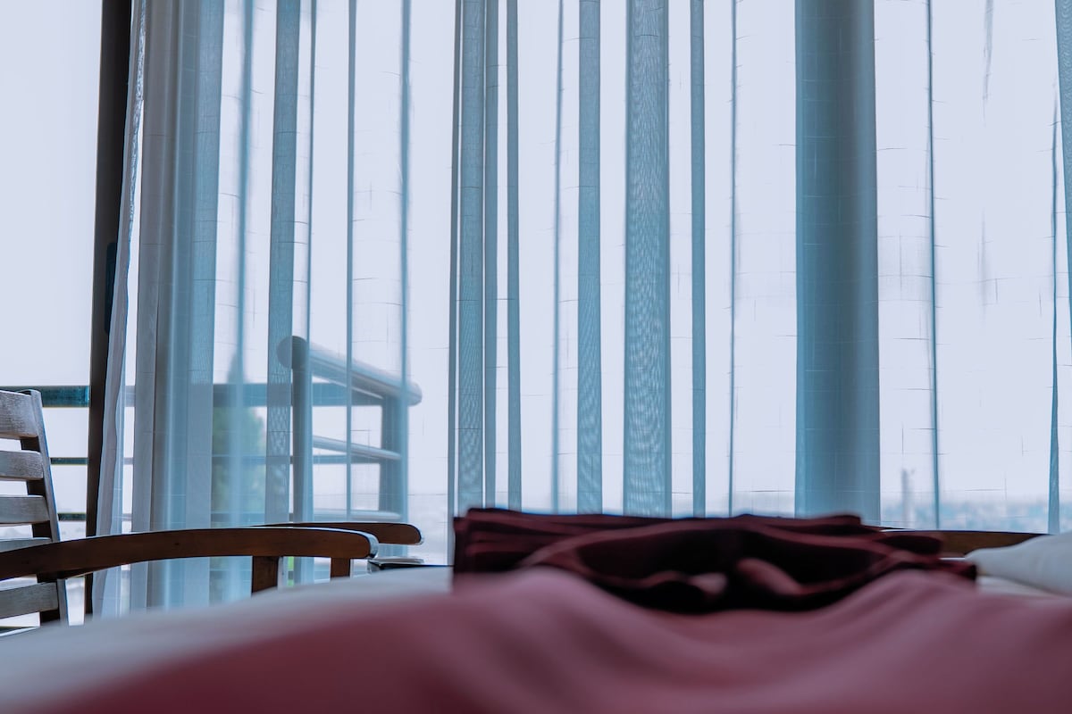 Una habitación de hotel con una cama, una silla y vistas a través de cortinas translúcidas.