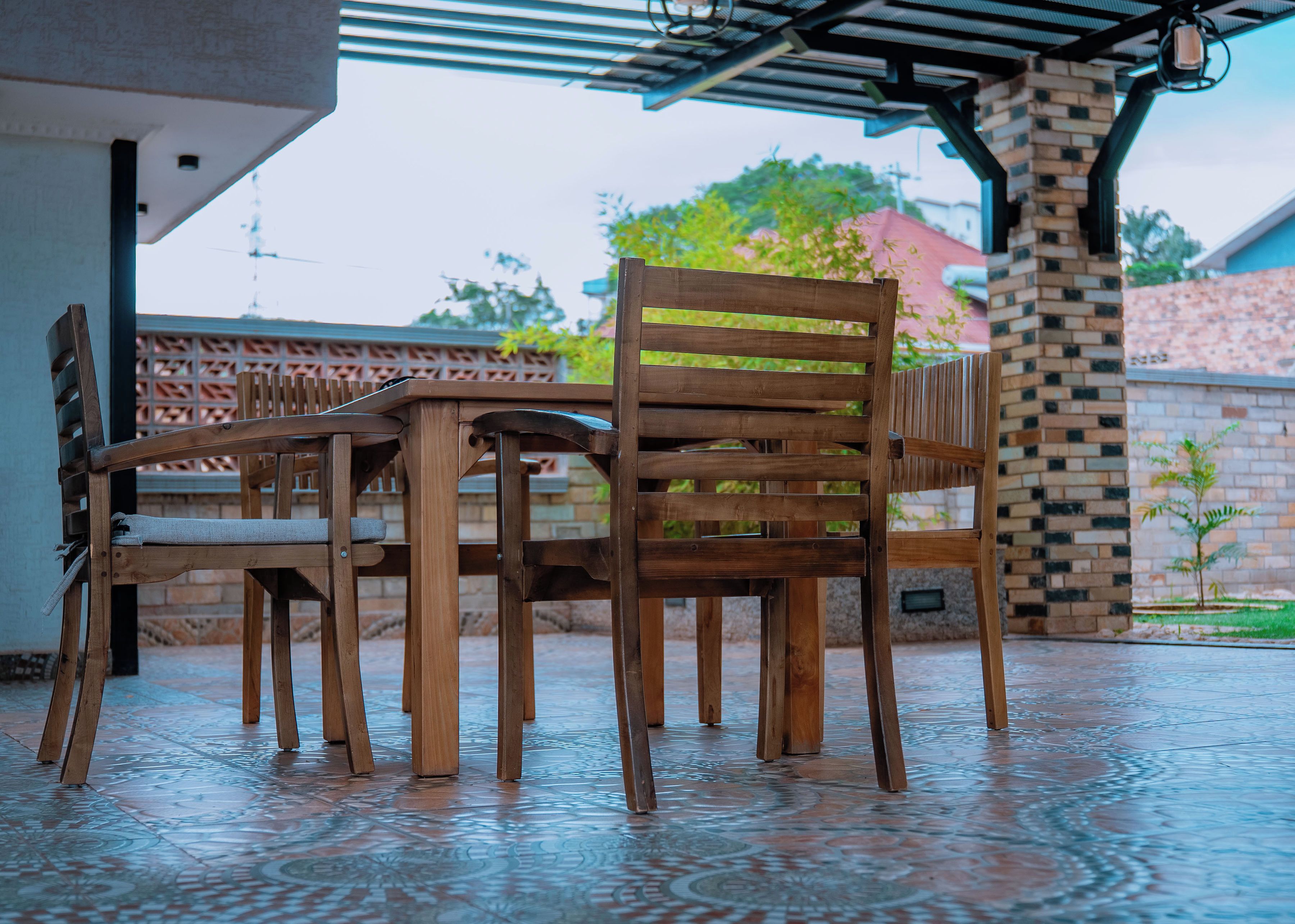 A covered outdoor seating area with wooden furniture and a patterned floor.