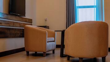 A room with two armchairs, a flat-screen TV mounted on the wall, a small table, and a window with curtains.