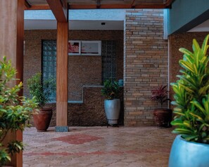 A covered outdoor area with tiled flooring, potted plants, and a brick wall.