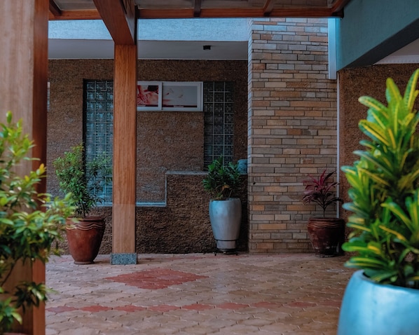 Un espacio al aire libre techado con suelo de baldosas, plantas en macetas y una pared de ladrillo.