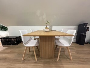 A rectangular wooden table with four white chairs, a small potted plant, and a black suitcase on the floor.