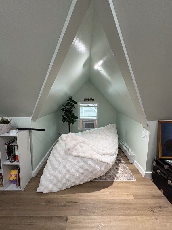 A bedroom with a sloped ceiling, a bed, a radiator, a plant, and a bookshelf.
