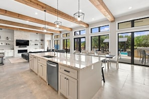 Cozinha moderna com uma ilha grande, vigas de madeira e vista para o exterior.