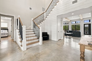 A spacious interior with a staircase leading to an upper level, a seating area with a sofa and table, and large windows providing natural light. - Lone Start Lookout@FrioRiverVactionRentals (Concan)