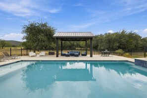 A clear swimming pool with lounge chairs and a covered seating area. - Lone Start Lookout@FrioRiverVactionRentals (Concan)