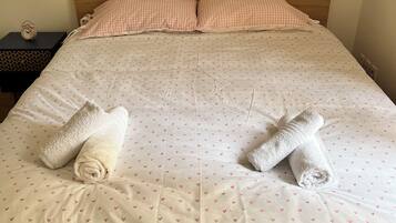 Een net opgemaakt bed met een geruit kussen, twee opgerolde handdoeken en een bedsprei met een patroon.