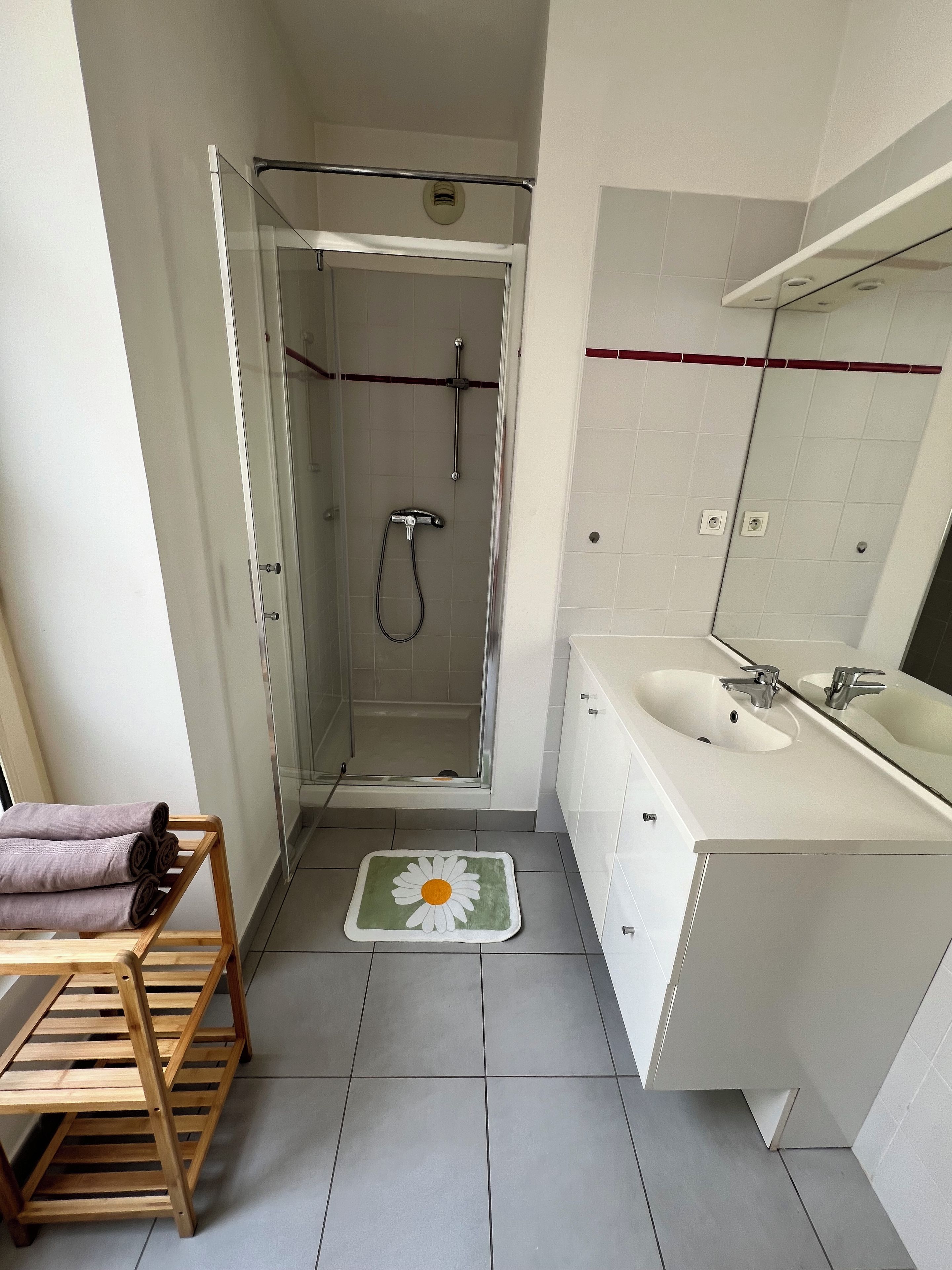Een badkamer met een douche, een wastafel en een houten plank met handdoeken.